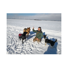 Joachim Ritz sitzt mit drei Hunden im Schnee und bewundert mit ihnen gemeinsam einen Schneeball.